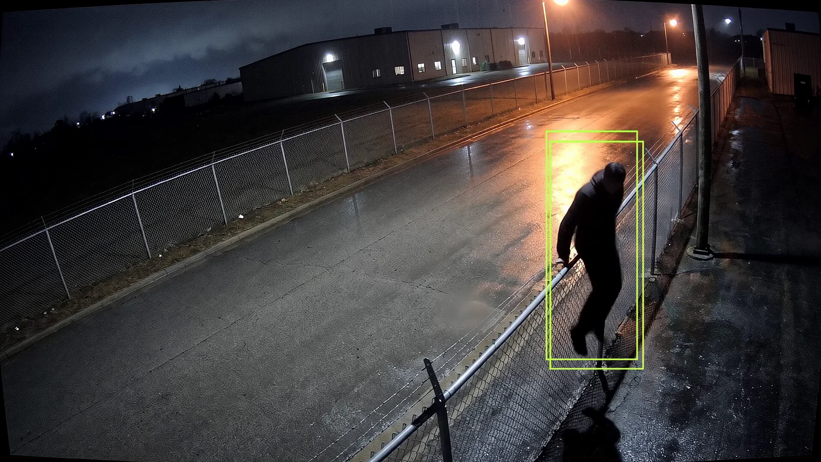 A figure crossing the perimeter fence beside the back gate at night.